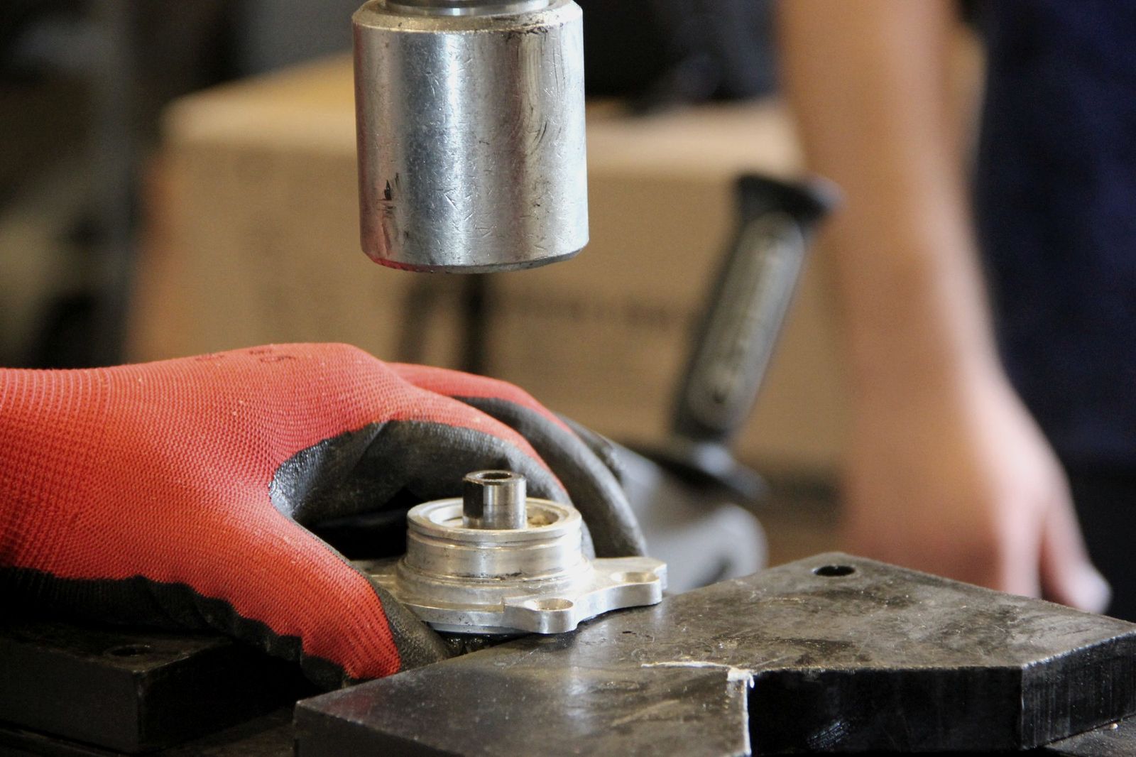 Illustrative photo: a gloved hand setting a machined metal part under a test instrument